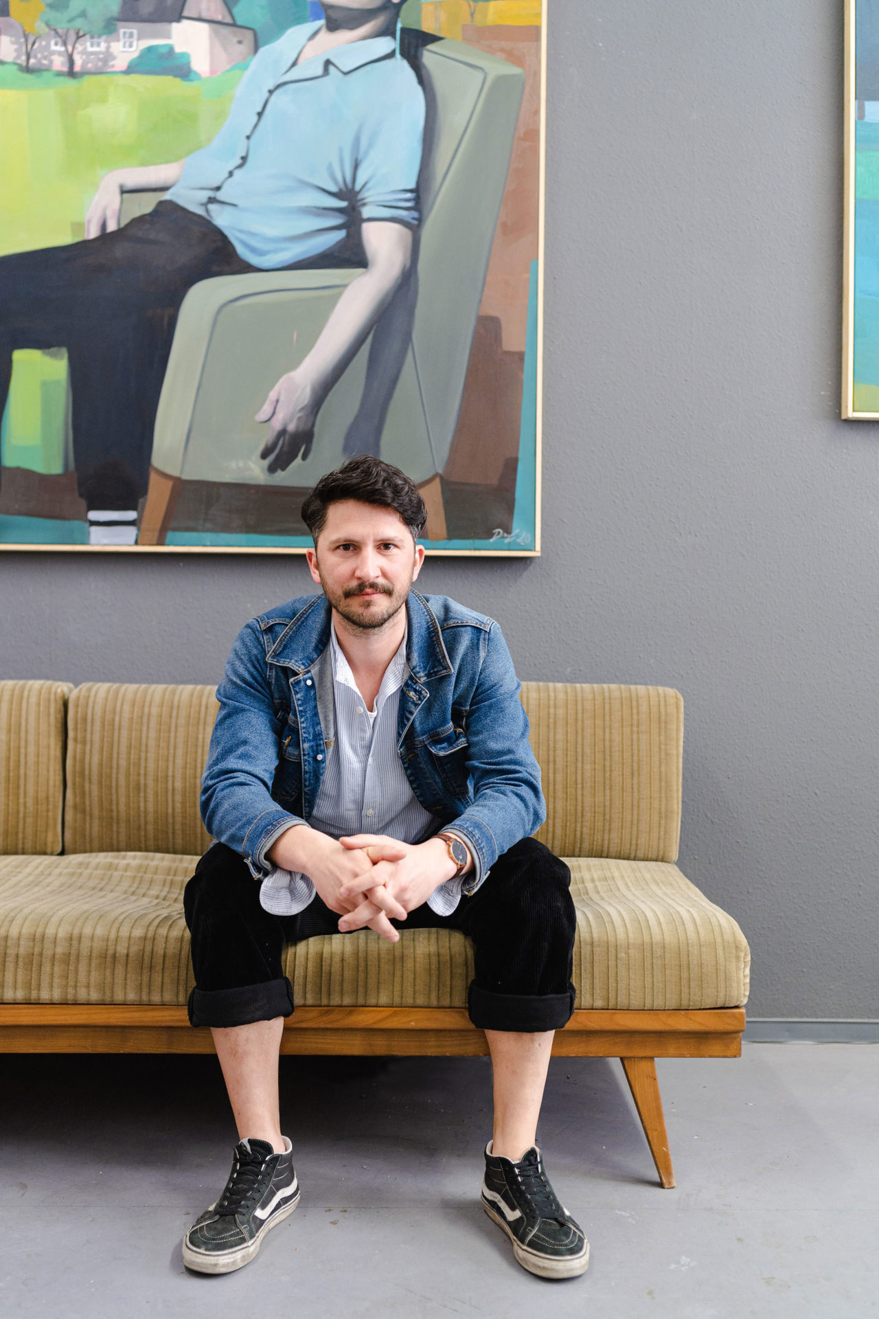 Künstler Jaroslav Drazil sitzt auf einer alten Couch vor seinen Bildern